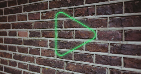 Composite of illuminated digital green play button icon against brick wall, copy space