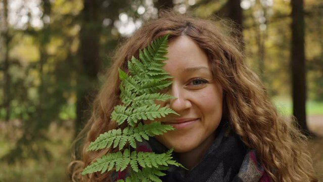 Portrait of a woman with flowing hair covers one half of her face with a fern leaf and smiles