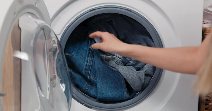 Close-up on the hands of a woman putting clothes into a washing machine. The filled interior of the drum, inserting laundry, closing the door and turning on the program.