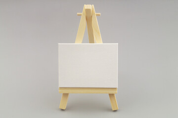 Wooden painting stand or easel with blank white canvas on gray background. 