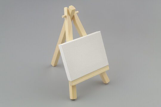 Wooden easel with blank canvas on gray background.