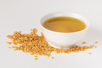 Close up of raw golden flax seeds  scattered on the table with linseed oil in a bowl, isolated