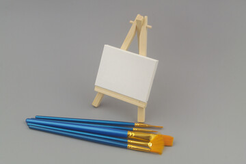 Many paintbrushes and easel with blank canvas on gray background. Creativity concept.