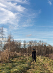 Young woman in dark coal and hat exploring autumn nature landscape standing backside