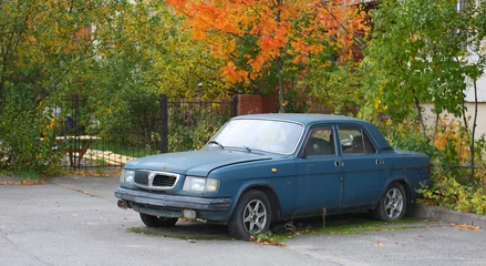 Deurstickers An old rusty blue car is parked near the autumn bush, Kollontai Street, St. Petersburg, Russia, October 2022 © Станислав Вершинин