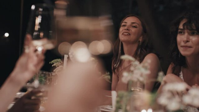 Group of people wearing stylish fancy outfits sitting at dining table spending great time relaxing at wedding party