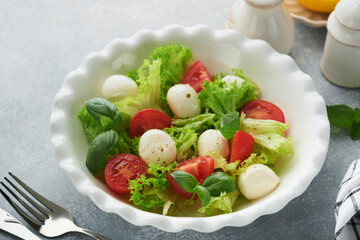 Caprese salad. Italian caprese salad with sliced tomatoes, mozzarella cheese, basil, olive oil in white plate over white background. Delicious Italian food. Top view. Rustic style.