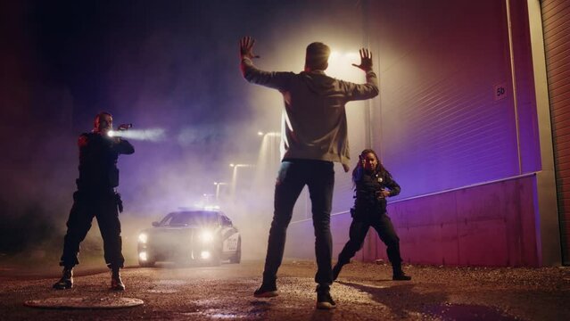 Two Police Officers Catch and Put Suspect Under Arrest. Cops Aiming Guns, Order Felon to Comply, Handcuff Dangerous Criminal on Dark City Street. Heroic Officers of the Law Fight Crime. Slow Motion