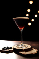 cocktail glass with dark drink and coffee bean ornaments on a black background with lights