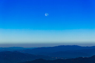 Moon and day in bright clouds before sunset. Moon in the blue sky. Moon and day with mountain. Day moon in summer time. Mountain and moon day with blue sky.