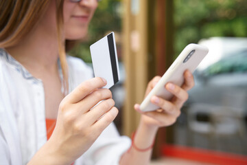 Closeup of the young smiling woman holding credit card using mobile phone shopping online, selective focus