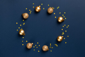Circle frame of golden Christmas balls and glitter confetti hearts on blue background with copy space