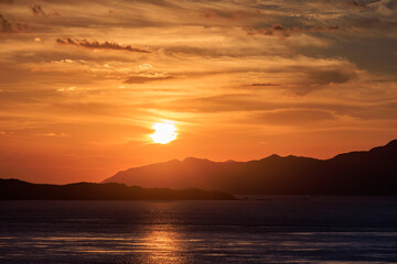 Low sun behind clouds at horizon over distant silhouetted mountains