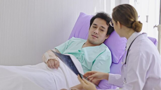 Caucasian female doctor explaining brain X-ray film to Asian male patient listening in hospital bed. Care by expert doctors. Diagnosis of neurodegenerative diseases a blood vessel in brain or cancer
