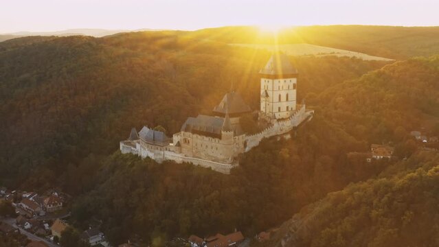 Market town and Karlstejn castle built on giant forestry hill at sunset. Wild nature and ancient architecture of Czeck Republic aerial view