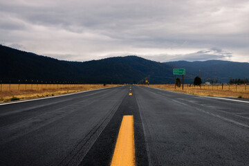 Empty road in America in a cloudy day. Empty road in California going through a yellow field with a view of the mountains in a distance