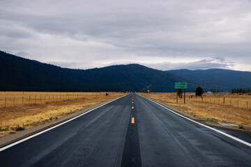 Empty road in America in a cloudy day. Empty road in California going through a yellow field with a view of the mountains in a distance - Powered by Adobe