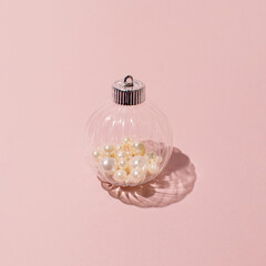 Transparent ball and pearls in it, creative Christmas decoration on a pastel pink background. Happy winter holidays idea. 