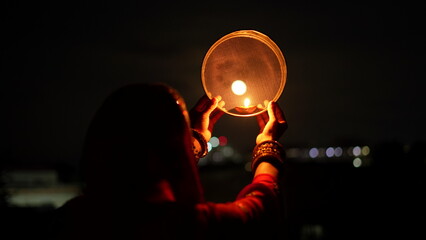 Woman hand holding Karwa Chauth strainer for the Karwa Chauth celebration on the night. Karwa Chauth strainer and Diya oil lamps for the Karwa Chauth celebration on the night