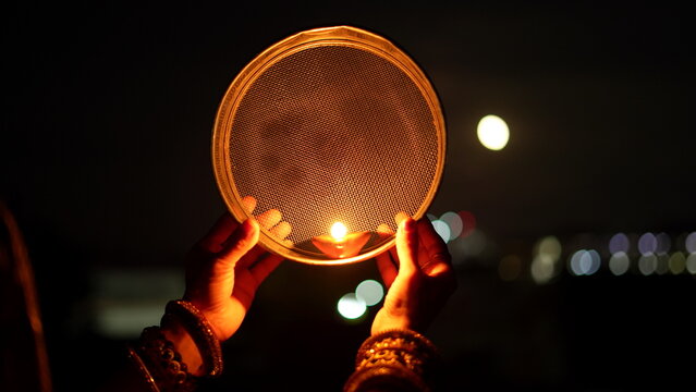 Woman hand holding Karwa Chauth strainer for the Karwa Chauth celebration on the night. Karwa Chauth strainer and Diya oil lamps for the Karwa Chauth celebration on the night