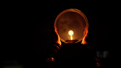 Woman hand holding Karwa Chauth strainer for the Karwa Chauth celebration on the night. Karwa Chauth strainer and Diya oil lamps for the Karwa Chauth celebration on the night