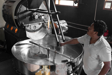 A Hispanic man is operating the lever of a coffee roaster machine