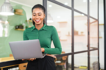 Smart and intelligent African-American businesswoman wearing smart casual shirt using laptop...