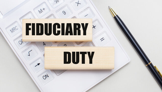 Wooden blocks with the FIDUCIARY DUTY Iie on a light background on a white calculator. Nearby is a black handle. Business concept
