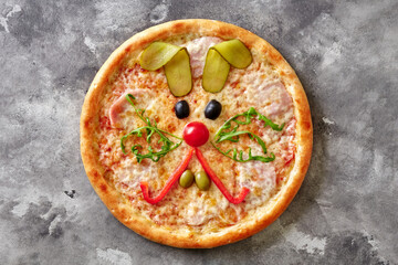 Funny pizza with mozzarella, ham and bunny muzzle of olives, cherry tomato, bell pepper, arugula and pickled cucumber