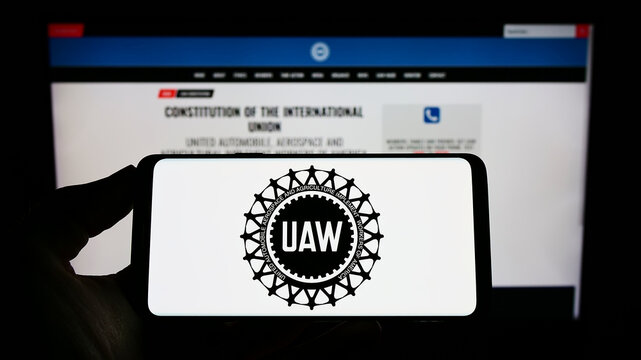 Stuttgart, Germany - 09-30-2022: Person holding cellphone with logo of American trade union United Auto Workers (UAW) on screen in front of webpage. Focus on phone display.