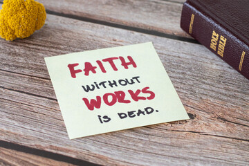 Faith without works is dead, a handwritten biblical note and a closed Holy Bible Book on a wooden...