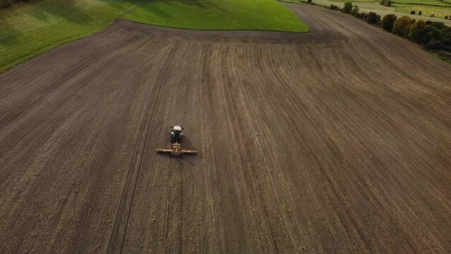 A tractor rolling a ploughed field in Autumn. High from behind.  Aerial