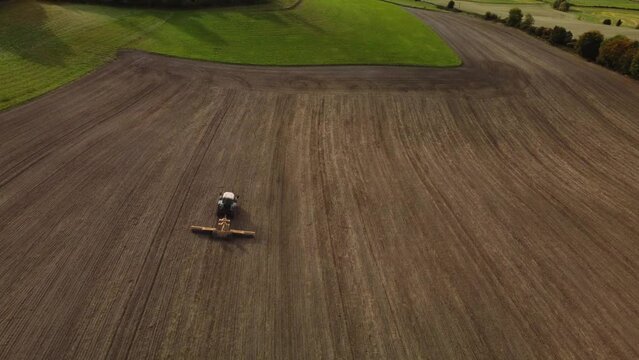 Following a tractor tractor rolling a ploughed field in Autumn.  Aerial