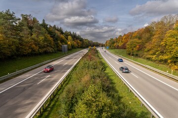 Cars are driving fast over a highway at the fall time, framed by beautiful trees, centred view.