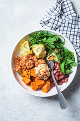 Winter vegan buddha bowl with tofu, beans, baked vegetables, hummus and beans.
