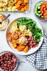 Winter vegan buddha bowl with tofu, beans, baked vegetables, hummus and beans.