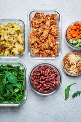 Vegan meal prep containers with  marinated tofu, beans, baked vegetables, green salad and vegetable sticks.
