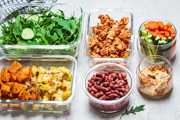 Vegan meal prep containers with  marinated tofu, beans, baked vegetables, green salad and vegetable sticks.