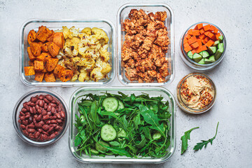 Vegan meal prep containers with  marinated tofu, beans, baked vegetables, green salad and vegetable...