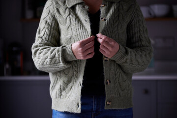 Woman Putting On Extra Jumper Clothing Trying To Keep Warm During Cost Of Living Energy Crisis
