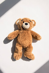 Soft toy bear lies under natural light on a white background. Top view, flat lay