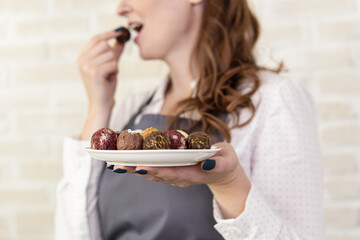 Woman in grey apron holds plate of chocolates. Soft focus. Professional pastry chef or chocolatier. Candy tasting