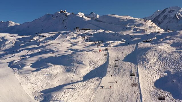 Zermatt, Switzerland: Aerial footage of the famous Zermatt ski resort with a chairlift and skiers and snowboarders on the slope of the Gornergrat ridge in the Swiss alps on a sunny winter day. 
