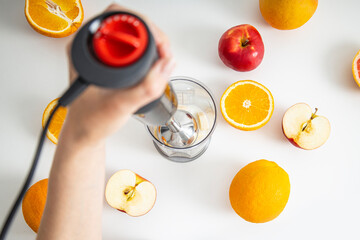 Female hands use a hand blender to mix fresh fruits to make a diet smoothie on a white background. Top view, flat lay