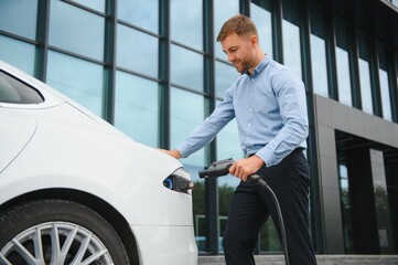portrait of young handsome bearded man in casual wear, standing at the charging station and holding...