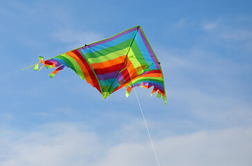 kite with multicolored stripes of the rainbow flies high in the blue sky tied to a string