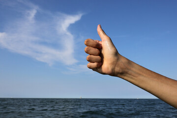 hand with thumb raised as a sign of success and the sea with the sky