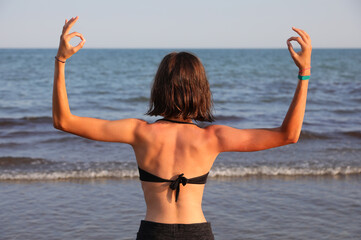 slender girl back to back while doing Yoga meditation exercises and doing OM symbol with hands
