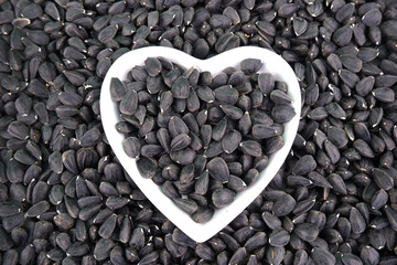 Black sunflower seeds lie on a white heart-shaped plate against the background of a sunflower seed.Seasonal sunflower harvest for export for oil production.