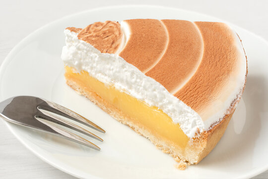 Single piece of lemon tart with meringue topping on a white plate next to a fork.